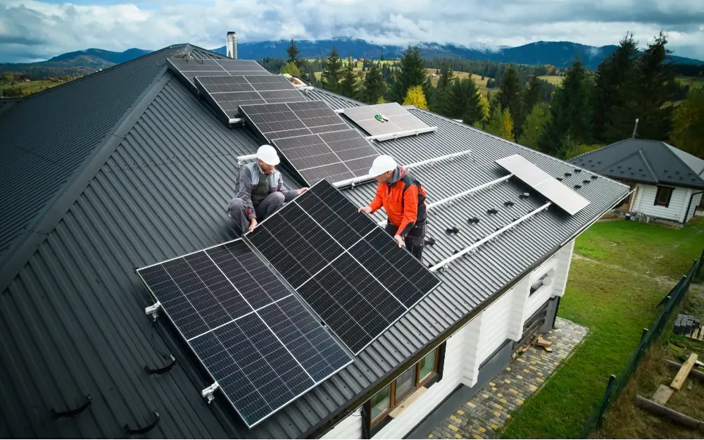 Two solar panel installers affixing solar panels on a racking system mounted on a residential home.