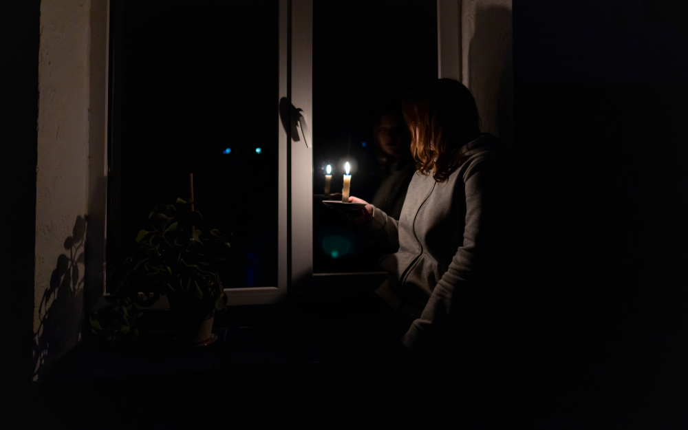 Person holding a lit candle near a window in a dark room.
