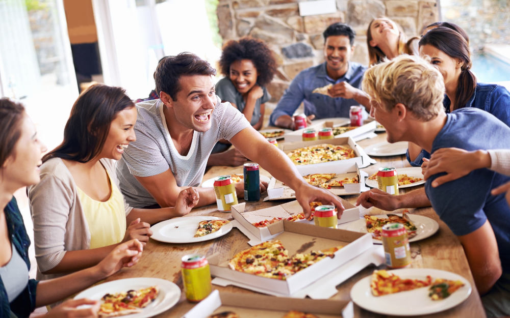 A group gathered around a table enjoying pizza and soda, laughing and sharing a meal together.